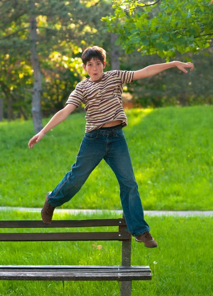 Rapaz adolescente feliz saltando do banco no parque — Fotografia de Stock