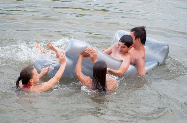 Adolescentes meninos e meninas se divertindo com um colchão no rio — Fotografia de Stock