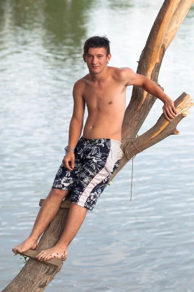 Teenage boy standing on the tree that leans over the river on beautiful summer day — Stockfoto