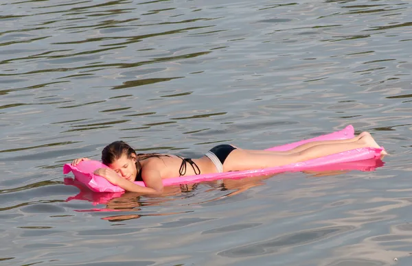 Милая девушка-подросток лежит на розовом матрасе, который плавает на поверхности моря — стоковое фото