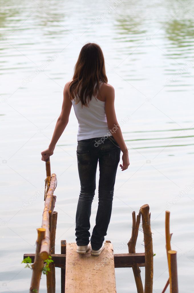 Beautiful lonely teenage girl standing on the edge of the river dock