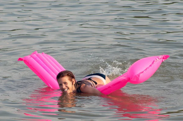Schattig tienermeisje liggend op de roze matras die op het zee-oppervlak drijft — Stockfoto
