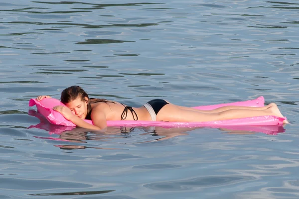 Cute teenage girl lying on the pink mattress that floats on the sea surface — Stock Photo, Image