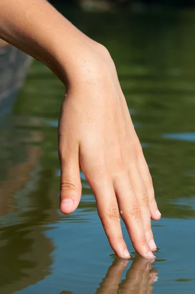 Γυναικείο χέρι αγγίζει επιφάνεια νερού σε ηλιόλουστη καλοκαιρινή μέρα — Φωτογραφία Αρχείου