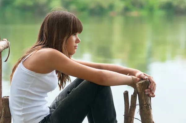 Pretty teenage girl sitting on the dock beside the river on beautiful summer day — Stock Photo, Image