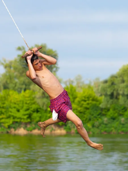 Menino adolescente pulando no rio de corda balançando no dia ensolarado de verão — Fotografia de Stock