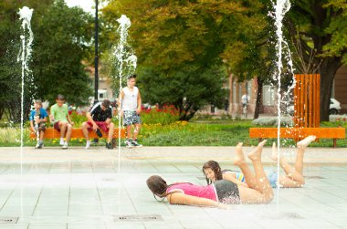 Teenage girls having fun in the towns water fountain on hot summer day clipart