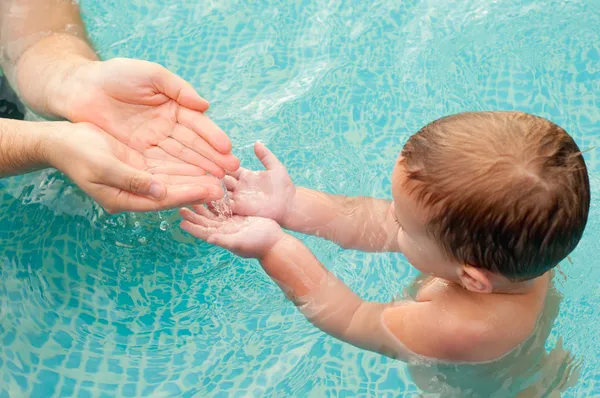 Padre vertiendo agua en las manos de su hijo en la piscina en el hermoso día de verano. El foco está en las manos —  Fotos de Stock