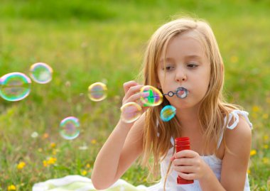 Cute little girl blowing soap bubbles on the meadow on sunny summer day clipart