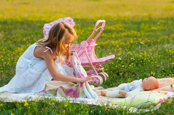 Carino bambina che gioca con il suo giocattolo bambino sul prato nella soleggiata giornata estiva — Foto Stock