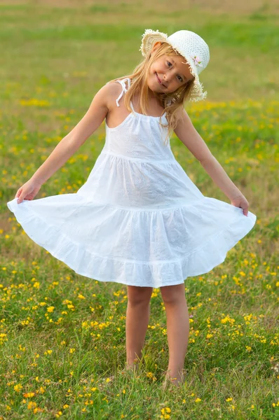 Cute little girl in white dress and hat walking on the meadow on sunny summer day — Stock Photo, Image