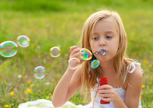 Cute dziewczynka dmuchanie baniek mydlanych na łące w słoneczny letni dzień — Zdjęcie stockowe