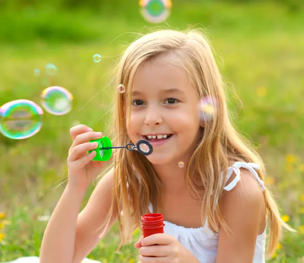 Cute little girl blowing soap bubbles on the meadow on sunny summer day — Stock Photo, Image