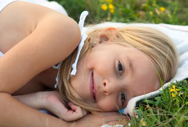 Roztomilý usměvavá holčička leží na dece na louce na krásné letní den — Stock fotografie