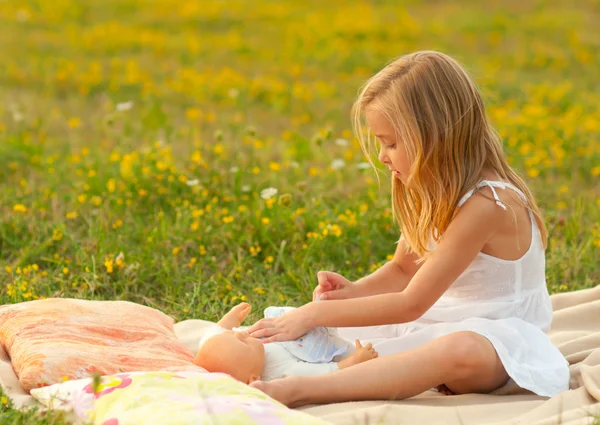 Çayır üzerinde onun bebek oyuncağı ile oynarken sevimli küçük kız — Stok fotoğraf