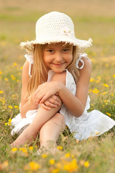 Aranyos kis lány ül a réten, napsütéses nyári napon — Stock Fotó