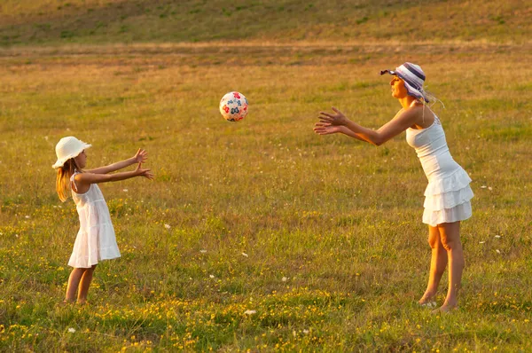 Мать и дочь бросают мяч друг другу на луг в солнечный летний день — стоковое фото