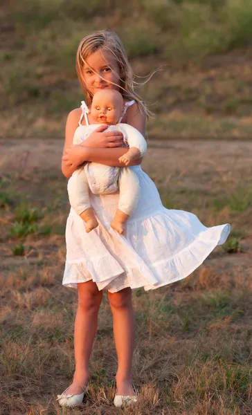 Triste menina de pé sozinha e segurando seu brinquedo bebê no dia ensolarado de verão — Fotografia de Stock