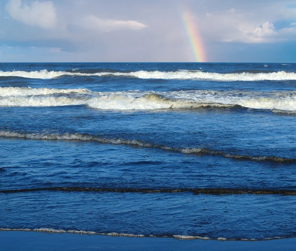 Κύματα του ωκεανού σπάσιμο στην ακτή με μια μερική ουράνιο τόξο στο υπόβαθρο — Φωτογραφία Αρχείου