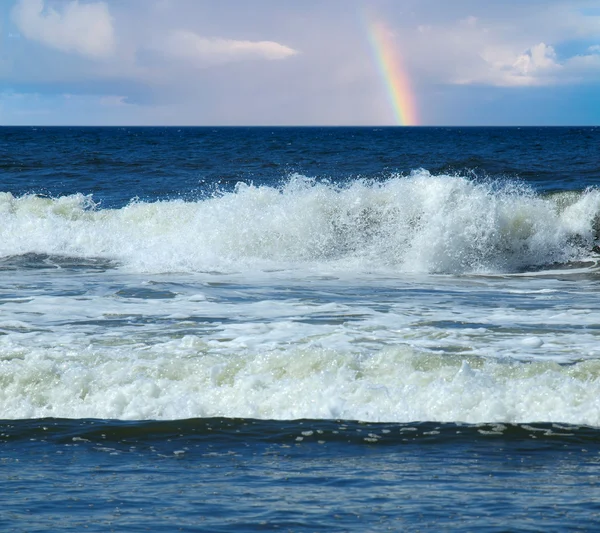 Onde oceaniche che si infrangono sulla riva con un arcobaleno parziale sullo sfondo — Foto Stock