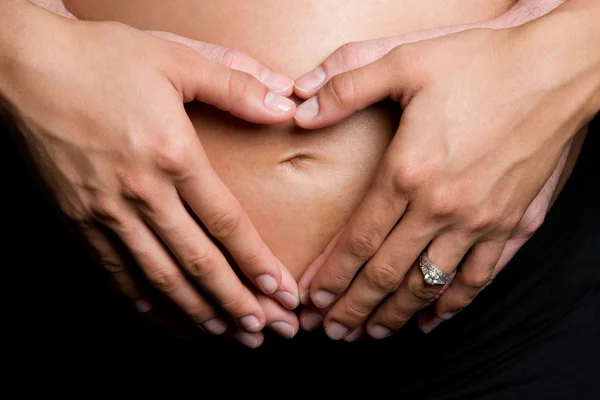 Mains formant le cœur sur le ventre enceinte — Photo