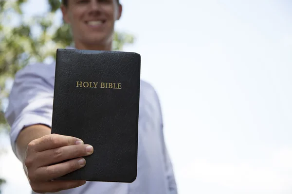 Junger Mann hält Bibel und lächelt — Stockfoto