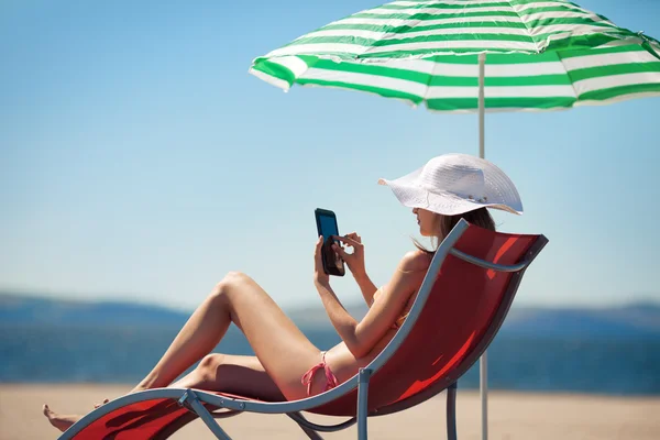 stock image Woman holding tablet computer sitting on the beach in deck chair