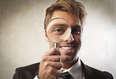 Young businessman looking through a magnifying glass clipart