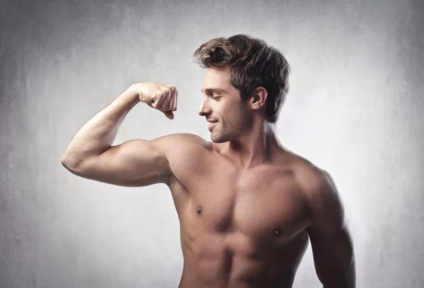 Uśmiechający się przystojny młodzieniec, pokazano jego biceps — Zdjęcie stockowe