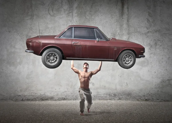 Muscular man holding a car in his hands — Stock Photo, Image