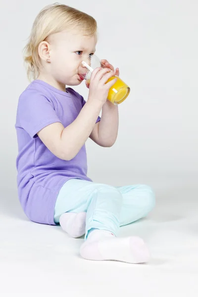 Mała dziewczynka pije sok pomarańczowy — Zdjęcie stockowe