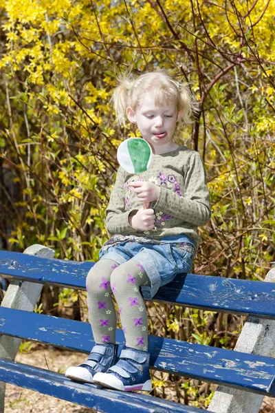 春のベンチに座っているロリポップと小さな女の子 — ストック写真
