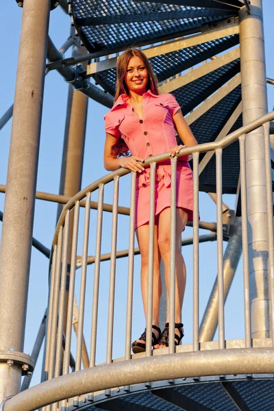 Νεαρή γυναίκα φοράει ροζ φόρεμα στέκεται στα σκαλοπάτια του η ρυμούλκηση επιφυλακή — Φωτογραφία Αρχείου