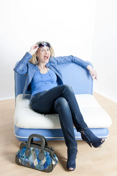 Kvinna klädd i blå kläder med handväska som sitter på soffan — Stockfoto