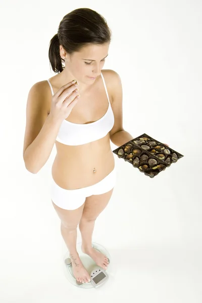 Γυναίκα, φορώντας εσώρουχα στέκεται με κουτί σοκολάτες σε κλίμακα βάρους — Φωτογραφία Αρχείου