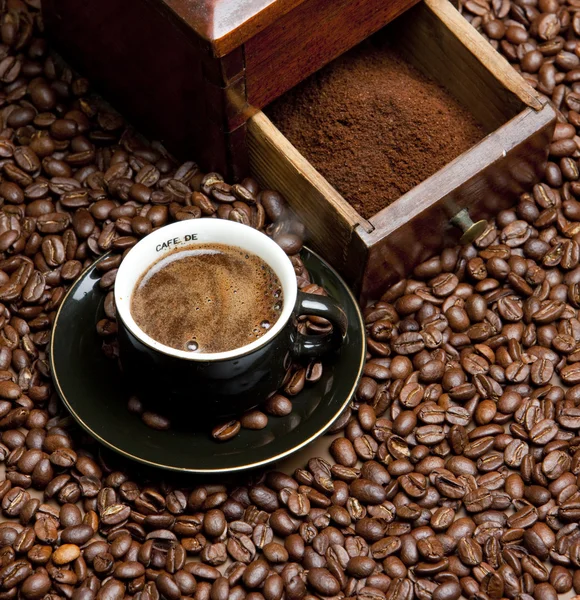Деталь кофейной мельницы с кофейными зёрнами и чашкой кофе — стоковое фото