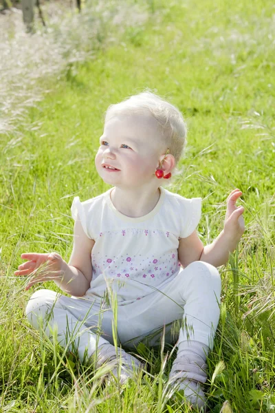 Маленька дівчинка з вишнями сидить на траві — стокове фото