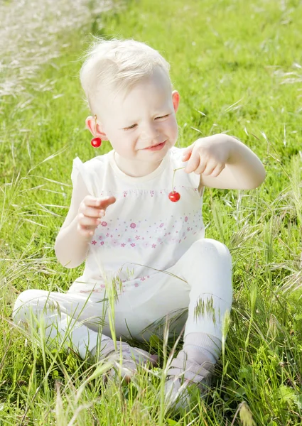 Dziewczynka z wiśniami, siedząc na trawie — Zdjęcie stockowe