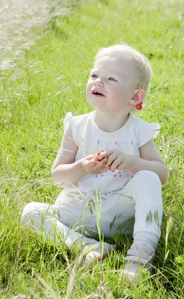 Маленька дівчинка з вишнями сидить на траві — стокове фото