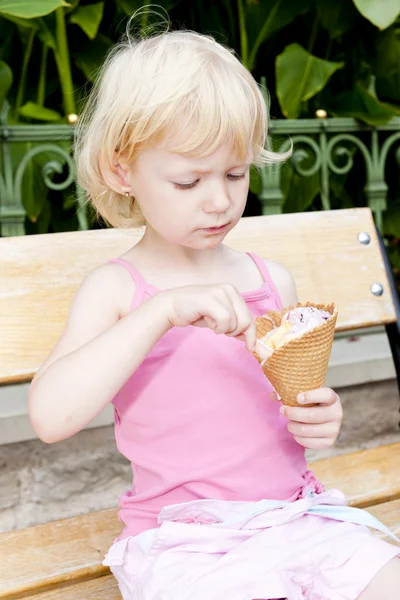 Маленькая девочка с мороженым сидит на скамейке — стоковое фото