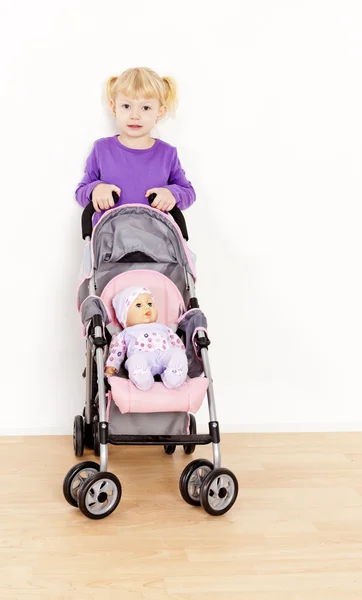 Liten flicka som leker med en docka och en barnvagn — Stockfoto