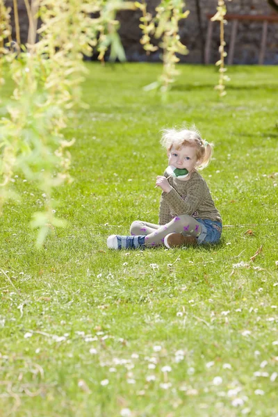 Niña con una piruleta sentada en la hierba —  Fotos de Stock
