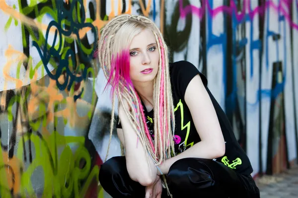 Portrait of young woman sitting at graffitti wall — Stock Photo, Image