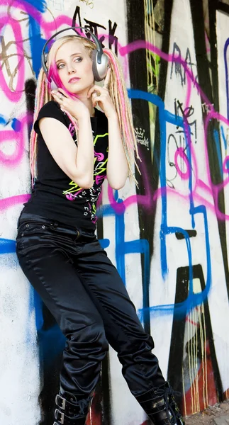 Młoda kobieta z słuchawkami na ścianie graffiti — Zdjęcie stockowe