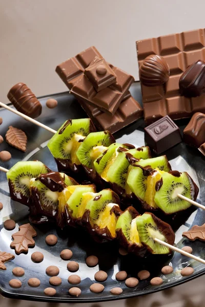 Fruit skewers and chocolate candies — Stock Photo, Image