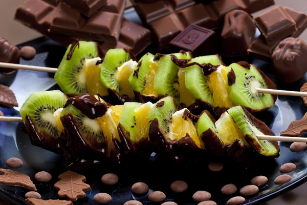 Fruit skewers and chocolate candies — Stock Photo, Image