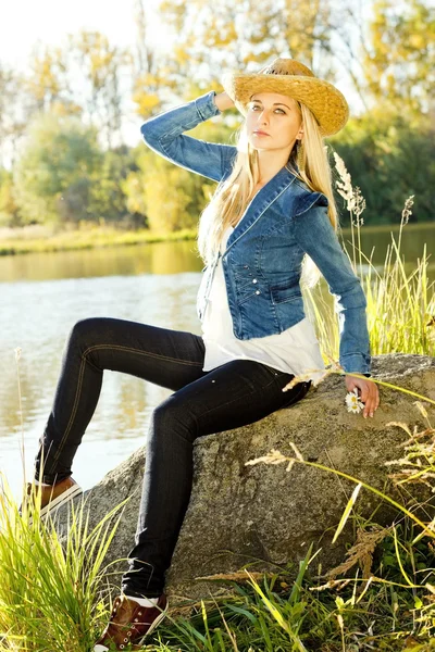Ung kvinna sitter på stenen vid dammen — Stockfoto
