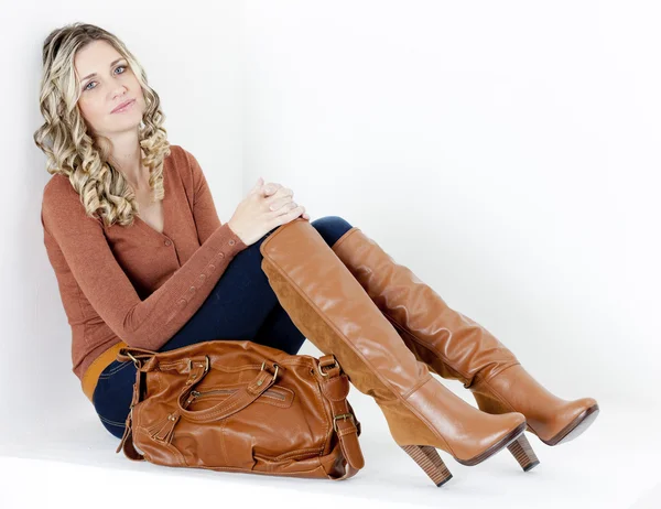 Sittande kvinna klädd i fashionabla bruna stövlar med en handväska — Stockfoto