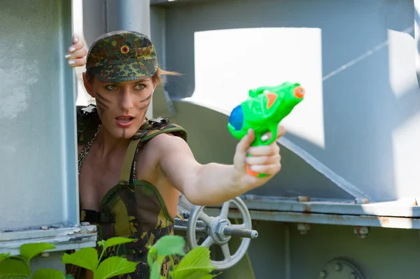 Woman in camouflage shoots from a water pistol — Stock Photo, Image