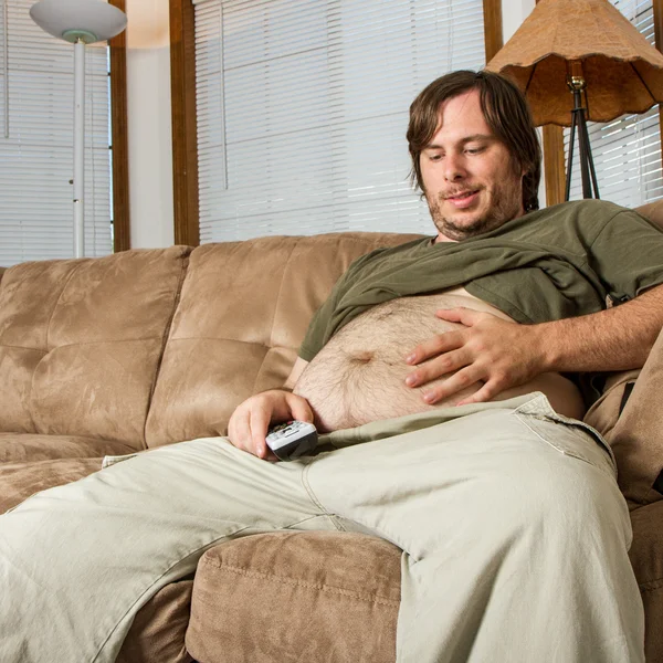 Pesado homem no sofá admirando seu estômago — Fotografia de Stock